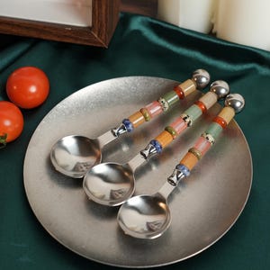 May include: Three stainless steel spoons with decorative handles featuring a series of stacked, multi-colored stone beads in shades of orange, green, pink, and blue, topped with a polished silver-toned metal sphere at the end of each handle.