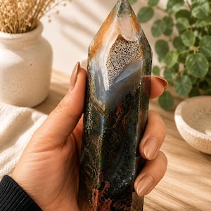 Puede incluir: Una torre de cristal hexagonal pulida que presenta una mezcla de tonos verde bosque profundo, marr&oacute;n terroso y &aacute;mbar transl&uacute;cido. La piedra muestra inclusiones complejas similares al musgo, bandas naturales y un &aacute;pice afilado y puntiagudo.