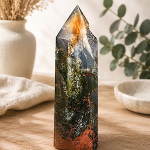 Puede incluir: Una torre de cristal pulido con una composici&oacute;n multicolor de inclusiones verde oscuro similares al musgo, dep&oacute;sitos minerales de color rojo anaranjado en la base y secciones grises transl&uacute;cidas con un &aacute;pice claro y caras lisas.