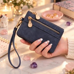May include: A navy blue rectangular wristlet wallet with a matte finish, featuring a gold-toned zipper closure, a matching detachable wrist strap, and two distinct gold-toned zipper pulls shaped like light bulbs attached to the front pocket.