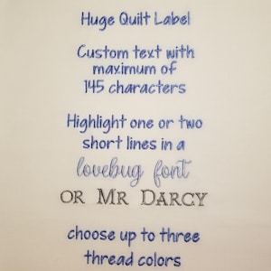 May include: A white fabric label with blue and brown embroidery. The text reads "Huge Quilt Label", "Custom text with maximum of 145 characters", "Highlight one or two short lines in a lovebug font OR MR DARCY", and "choose up to three thread colors".