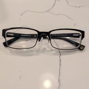 May include: Black Emporio Armani eyeglasses with rectangular frames. The inner temple features the text Emporio Armani and CE, while the other side displays EA 1036 3109 53 17 140. A small gold-tone logo is visible on the temple tip.