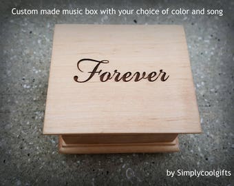 May include: A wooden music box with the word "Forever" engraved on the top. The box is made of light wood and has a simple design.
