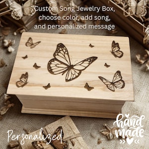 May include: A wooden jewelry box with a butterfly design. The box is light-colored with engraved butterflies on the lid. Text on the lid reads "Custom Song Jewelry Box, choose color, add song, and personalized message". The box is labeled "Hand Made" and "Personalized".