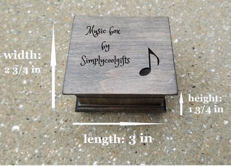 Pode incluir: Uma caixa de m&uacute;sica de madeira cinzenta com um desenho de nota musical e o texto "Music box by Simplycoolgifts". A caixa mede 7 cm de largura, 7,6 cm de comprimento e 4,4 cm de altura.