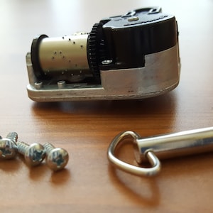 May include: A silver music box mechanism with a black winding key, four silver screws, and a silver winding key with a loop.