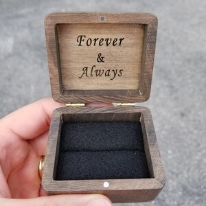 Pu&ograve; includere: Una scatola per anelli in legno con un interno in velluto nero. Il coperchio &egrave; aperto e l'iscrizione "Forever & Always" &egrave; visibile.
