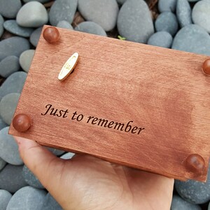 Puede incluir: Una caja de m&uacute;sica de madera con una llave de cuerda dorada. La caja est&aacute; grabada con las palabras "Just to remember".