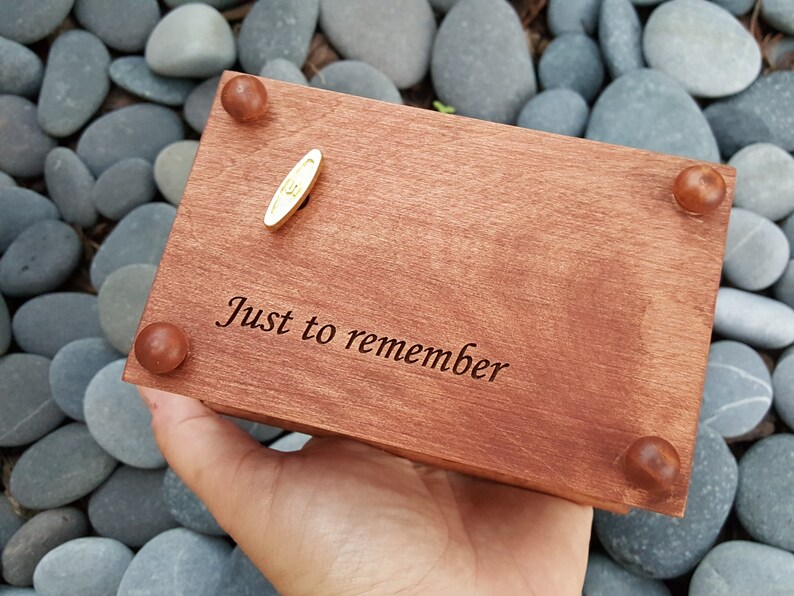 Puede incluir: Una caja de m&uacute;sica de madera con una llave de cuerda dorada. La caja est&aacute; grabada con las palabras "Just to remember".