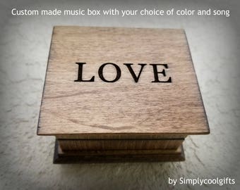 May include: A wooden music box with the word "LOVE" engraved on the top. The box is made of light brown wood and has a simple design.