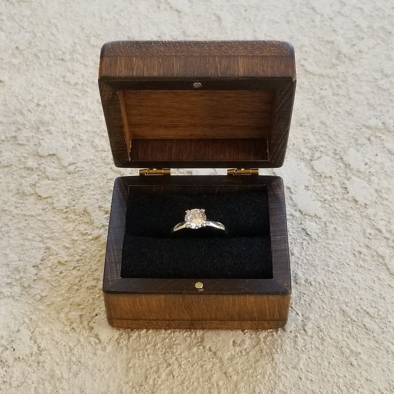 Pu&ograve; includere: Una scatola di legno per anelli con un interno in velluto nero. Un anello di diamanti &egrave; esposto nella scatola.