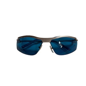 May include: Protective eyewear featuring a sleek, metallic silver frame and dark blue tinted lenses. The glasses have a wrap-around design with a single continuous brow bar and adjustable nose pads, providing full coverage for the eyes.