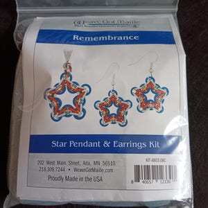 May include: A clear plastic bag containing a Star Pendant & Earrings Kit. The kit features a star-shaped pendant and earrings with red, white, and blue chainmaille. The text "Remembrance" is above the star design. The kit is proudly made in the USA.
