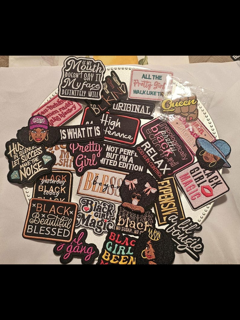 May include: A collection of embroidered fabric patches featuring various motivational and expressive phrases in black, pink, white, and gold thread. The patches include illustrations of faces, lips, and crowns, with text such as Black Girl Magic, Pretty Girl, and High Maintenance.