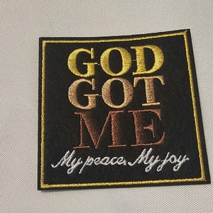 May include: A square black embroidered patch with a gold border. The text "GOD GOT ME" is stitched in a gold to bronze gradient, and the text "My peace. My joy." is stitched in white cursive script below the main lettering.