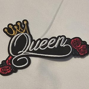 May include: An embroidered patch featuring the word Queen in white cursive script with a black background. A gold crown sits above the letter Q, and two red roses with green leaves are positioned at the bottom left and the far right of the text.