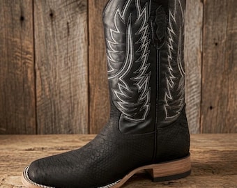 May include: A black leather cowboy boot featuring a textured snakeskin-patterned vamp and a tall shaft adorned with intricate white decorative stitching. The boot includes a stacked wooden heel and a light-colored welt with white stitching detail.