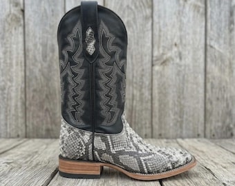 May include: A western-style boot featuring a black leather shaft with intricate grey stitching and a snakeskin-patterned foot. The boot has a square toe, a stacked wooden heel, and a pull tab at the top of the shaft with a snakeskin inlay.