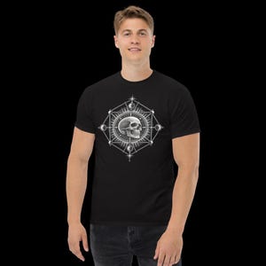 以下が含まれることがあります： 胸元に白いグラフィックプリントが施された黒の半袖Tシャツ。デザインは、線、星の模様、そして各角にある小さな円形の球体で構成された幾何学的なフレームの中心に、人間の頭蓋骨が配置されています。