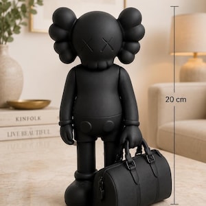 Può includere: Una statuetta da collezione nero opaco con occhi a forma di X e orecchie arrotondate, alta 20 cm. La figura tiene in mano una piccola borsa da viaggio nera. Il design presenta una finitura liscia e arti articolati con un aspetto stilizzato.