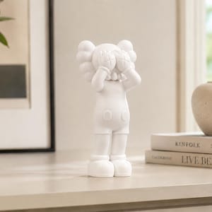 Può includere: Una statuetta da collezione in vinile bianco opaco che raffigura un personaggio ispirato ai cartoni animati con occhi a forma di X, in piedi con le mani che coprono il volto. Il personaggio ha orecchie arrotondate, pantaloncini con due bottoni e scarpe grandi.