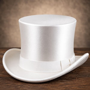 Puede incluir: Un sombrero de copa blanco sólido con un acabado suave similar al satén y una banda de cinta de grosgrain blanca a juego que rodea la base de la copa. El sombrero tiene una copa cilíndrica alta y un ala ancha y curva en todos los lados.