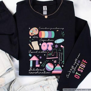 May include: A black long-sleeve sweatshirt featuring a colorful graphic print of occupational therapy tools and text including Executive functioning, Cognition, Visual motor, and Bilateral coordination. The sleeve displays the text Can't talk right now Doing OT STUFF.