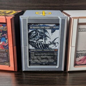 Könnte beinhalten: Drei rechteckige Kartenaufbewahrungsboxen mit Sichtfenstern. Die linke Box ist kupferfarben mit Kefka, Court Mage. Die mittlere Box ist silber mit Jin-Gitaxias, Core Augur. Die rechte Box ist weiß mit Lightning, Azorius Renegade.