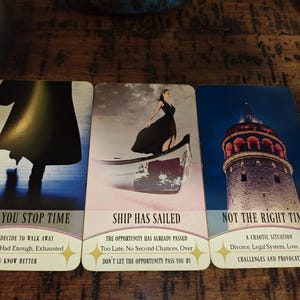 May include: Three rectangular oracle cards arranged side-by-side. The first card shows a silhouette in a coat with the text WHEN YOU STOP TIME. The second card depicts a person in a black dress on a boat with the text SHIP HAS SAILED. The third card shows a stone tower with the text NOT THE RIGHT TIME.