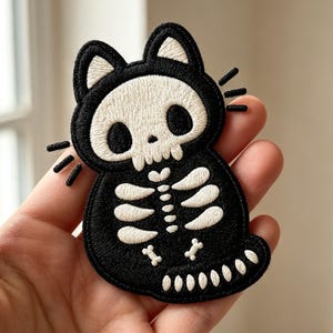 May include: An embroidered patch featuring a black cat silhouette with a white skull face and a white ribcage skeleton design. The cat has pointed ears, three whiskers on each side, and a tail with white bone segments along the bottom edge.
