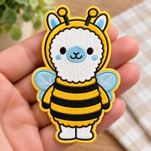 May include: An embroidered patch featuring a white llama character wearing a yellow and black striped bee costume with light blue wings, antennae, and a blue snout, finished with a yellow border and black stitching details.