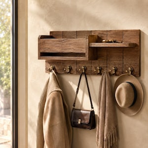 May include: A wall-mounted wooden organizer featuring a rectangular storage bin and a flat shelf. The unit includes six brass-toned metal hooks along the bottom edge for hanging items. The wood has a dark, textured finish with vertical paneling.