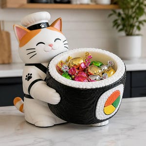 Puede incluir: Una figura de gato blanco y naranja vestido de chef, con un gorro blanco con una huella de pata, sosteniendo un gran cuenco con forma de sushi relleno de caramelos envueltos de colores. El sushi muestra arroz blanco, alga negra y un relleno colorido.