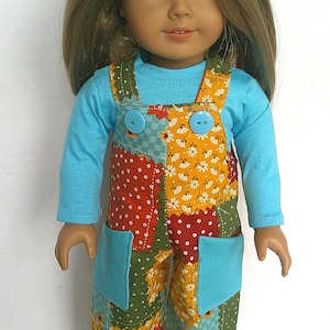 May include: A doll with long blonde hair wearing a light blue long-sleeve shirt under patchwork overalls. The overalls feature a multi-colored pattern of flowers and geometric shapes in orange, red, green, and blue, with two light blue pockets.