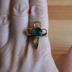 May include: A gold ring with a green gemstone set in a bow design.