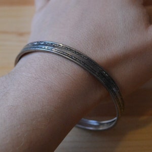 May include: A silver bangle bracelet with a decorative etched design.