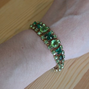 May include: A gold bracelet with a row of green and light green square-shaped rhinestones.