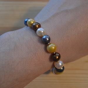 May include: A bracelet made of pearls in shades of gold, brown, white, and gray.