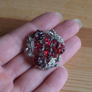 May include: A silver brooch with a cluster of red glass flowers and clear rhinestones.