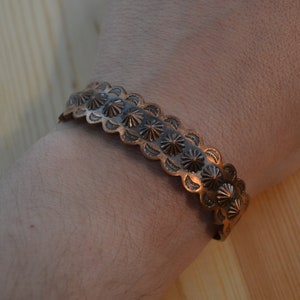 May include: A copper bracelet with a decorative design of repeating starburst patterns.