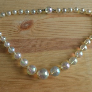May include: A white iridescent beaded necklace with a clasp closure. The beads are round and have a pearlescent finish.