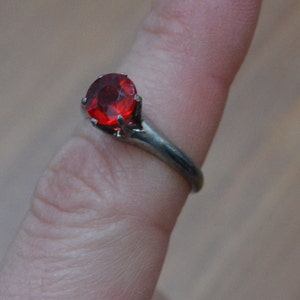 May include: A silver ring with a red gemstone set in a prong setting.