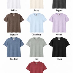 K&ouml;nnte beinhalten: Eine Comfort Colors 1717 Farbkarte mit zehn kurz&auml;rmeligen T-Shirts in verschiedenen Farbt&ouml;nen: Wei&szlig;, Elfenbein, Pfeffer, Espresso, Chambray, Orchidee, Blue Jean, Bay, Schwarz und Karmesinrot. Jedes T-Shirt hat einen Rundhalsausschnitt.