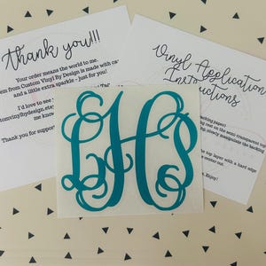 May include: A teal monogram vinyl decal with the letters "JH" in a decorative script. The decal is centered on a white square. Two white cards with handwritten text, including "Thank you!!!" and "Vinyl Application Instructions", are in the background.