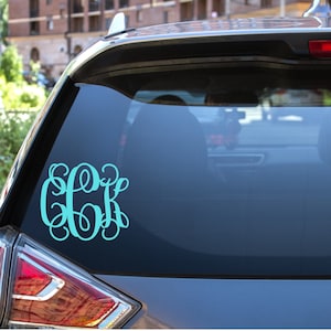 May include: A teal blue monogram decal with the letters "CK" in a cursive font, applied to the rear window of a silver car.