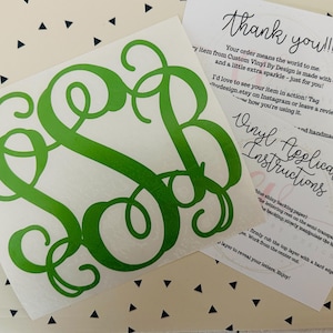 May include: A green monogram vinyl decal on a white backing, with a cursive font. Accompanying the decal are two cards with handwritten text: "Thank you!!!" and "Vinyl Application Instructions."
