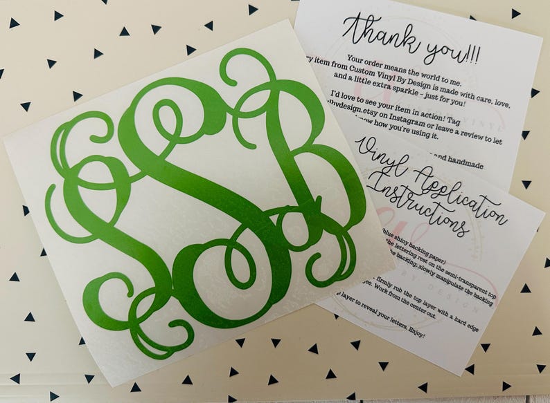 May include: A green monogram vinyl decal on a white backing, with a cursive font. Accompanying the decal are two cards with handwritten text: "Thank you!!!" and "Vinyl Application Instructions."