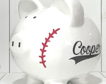 Puede incluir: Hucha de cerámica blanca con forma de cerdo, con diseño de béisbol. Presenta un gráfico de costura de béisbol roja y el nombre "Cooper" en escritura negra. El banco tiene cuatro patas pequeñas y dos orejas.