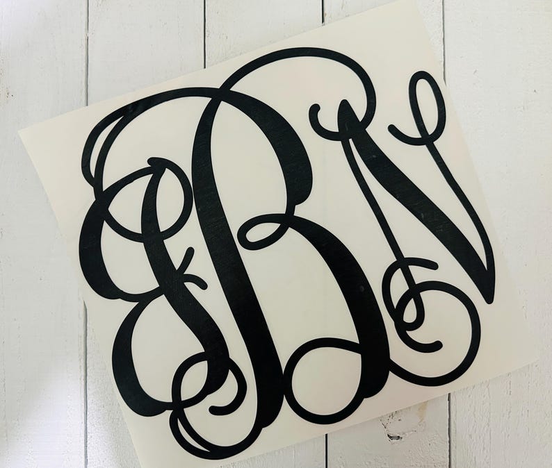 May include: Black monogram decal featuring the letters RBN in a classic, elegant script. The decal is on a white background, with a glossy finish. The design is suitable for various applications, such as car windows, laptops, or home decor.