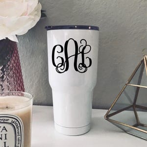 May include: White stainless steel tumbler with a black monogram of the letters "GAI".